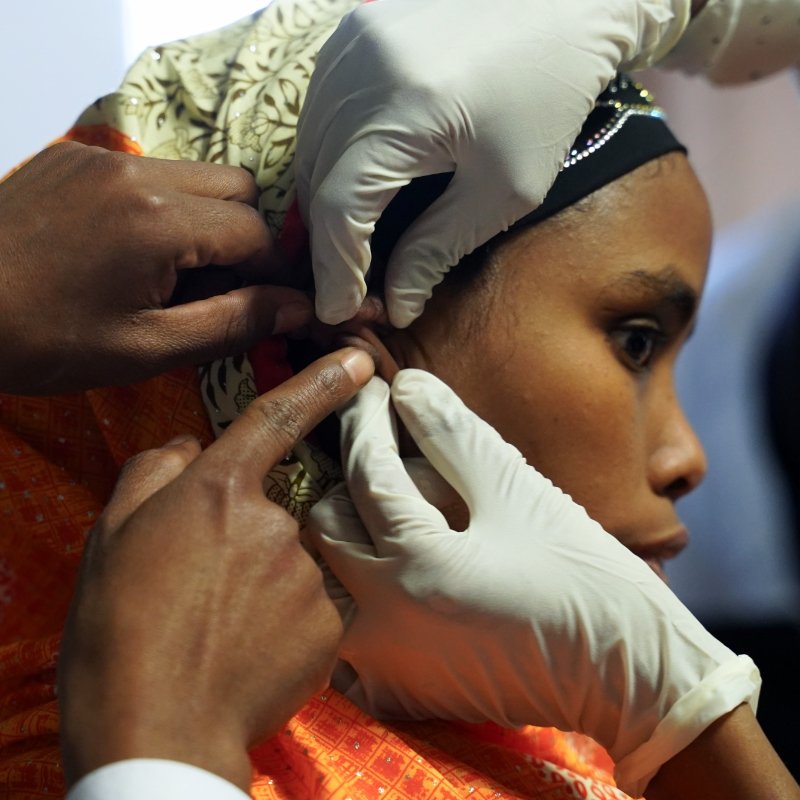 A woman with a hair covering is having her ear examined by two doctors