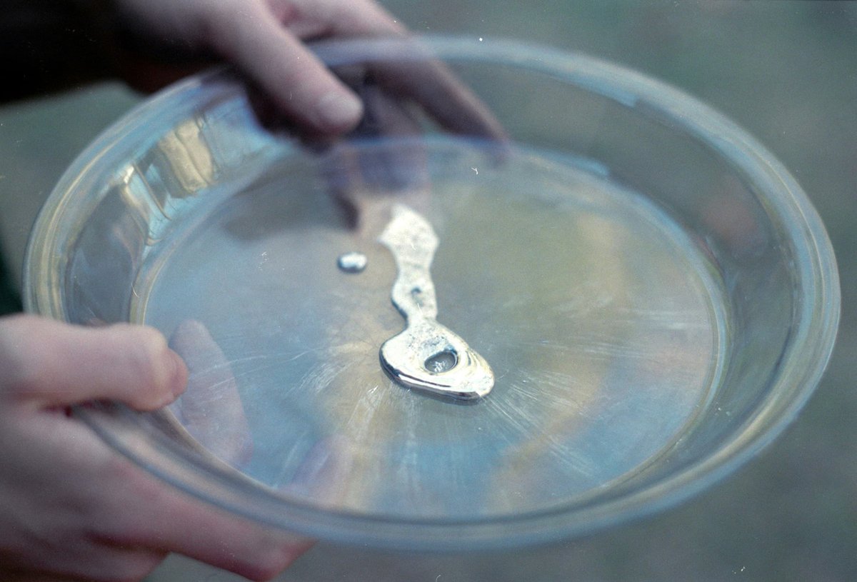 A pair of hands hold a plastic bowl with some liquid mercury in it.